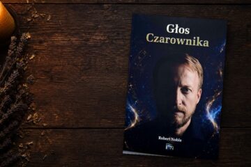 Okładka książki Głos Czarownika Roberta Noble na drewnianym stole przy świecy